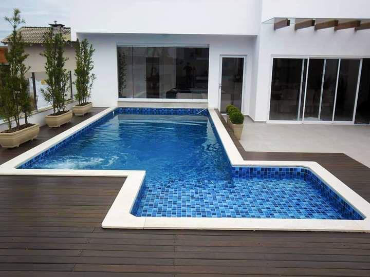 Piscina em formato recortado com revestimento em azulejo azul e prainha rasa, contornada por deck de madeira escura em residência branca.