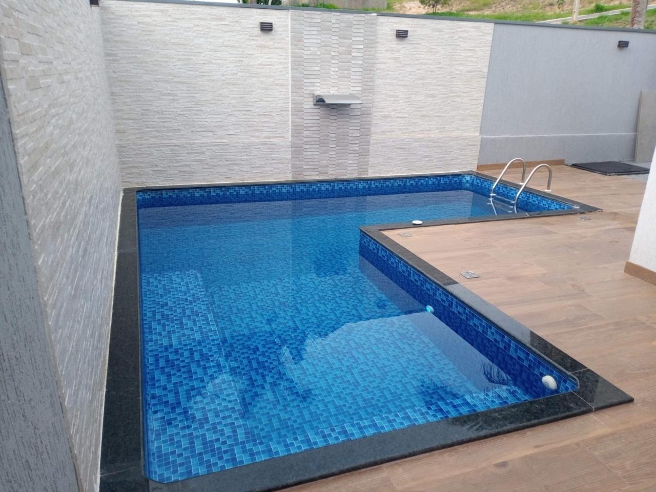 Piscina de alvenaria com revestimento em pastilha azul, borda em granito preto e prainha, com cascata na parede de pedra.